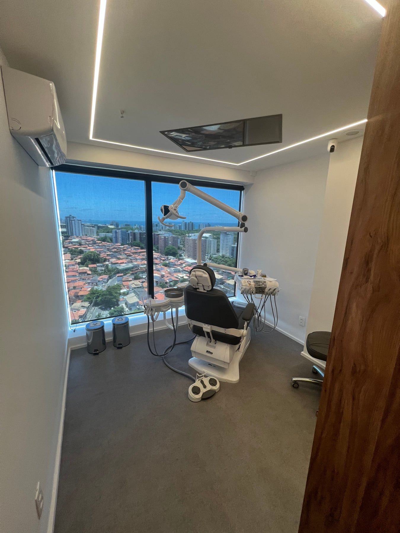 Sala clínica com cadeira odontológica e janela panorâmica sobre a cidade